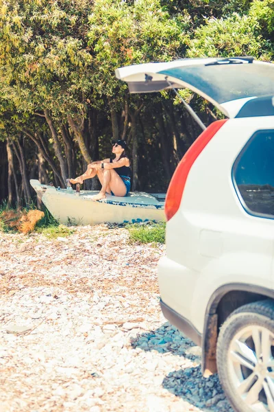 young woman sitting on boat at beach near car