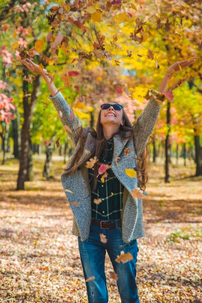 Junge hübsche Frau spielt mit gelben Herbstblättern im Stadtpark — Stockfoto