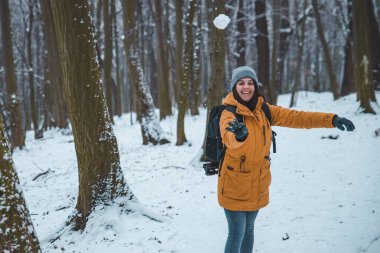 Gülümseyen genç bir kadın ormanda kartopu atıyor.