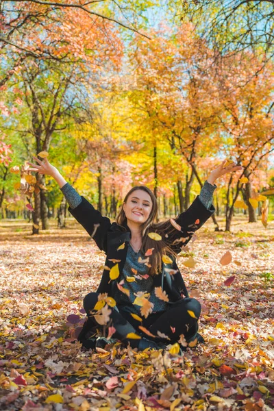 Młoda ładna kobieta bawi się żółtymi jesiennymi liśćmi w parku miejskim — Zdjęcie stockowe