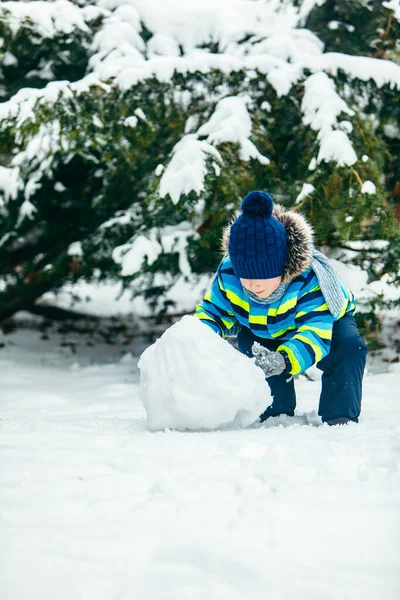 Kleine schattige jongen die sneeuwman maakt. rollen grote sneeuwbal — Stockfoto
