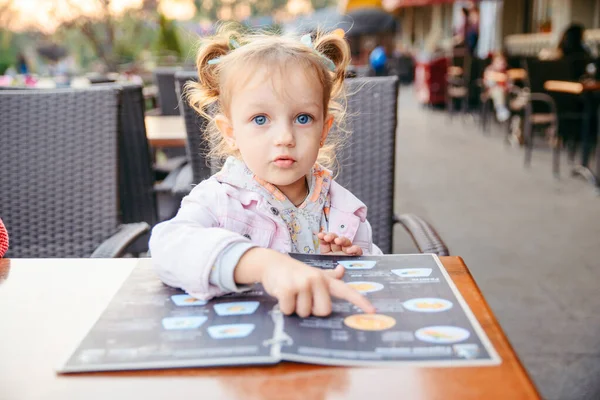 Niña sentada en la cafetería eligiendo comida del menú —  Fotos de Stock