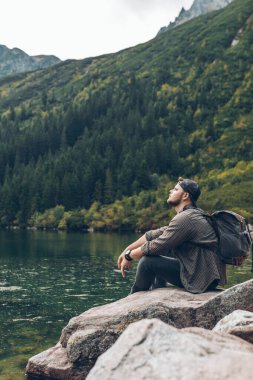 man sitting on the rock in front of lake in mountains enjoying the view