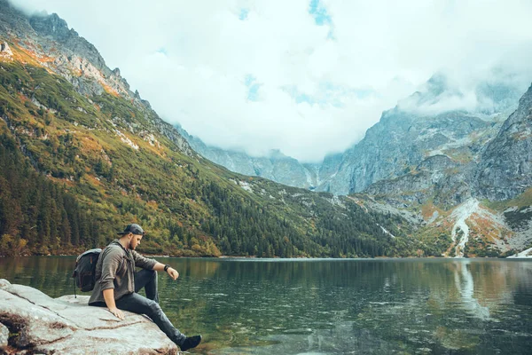 Man sitting on the rock in front of lake in mountains enjoying the view — Stock fotografie