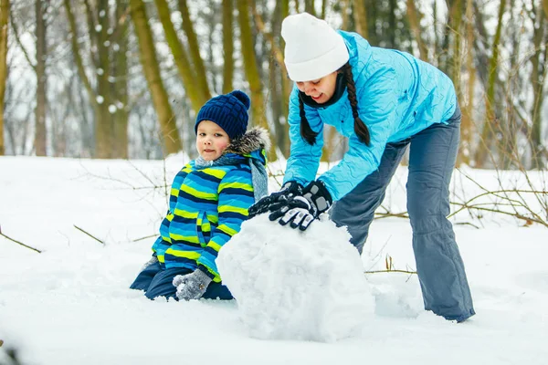 Mamma med småbarn son gör snögubbe. rullande stora snöboll — Stockfoto