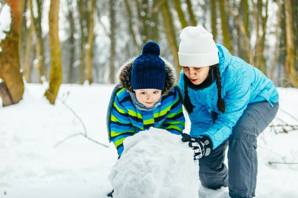Mamma med småbarn son gör snögubbe. rullande stora snöboll — Stockfoto