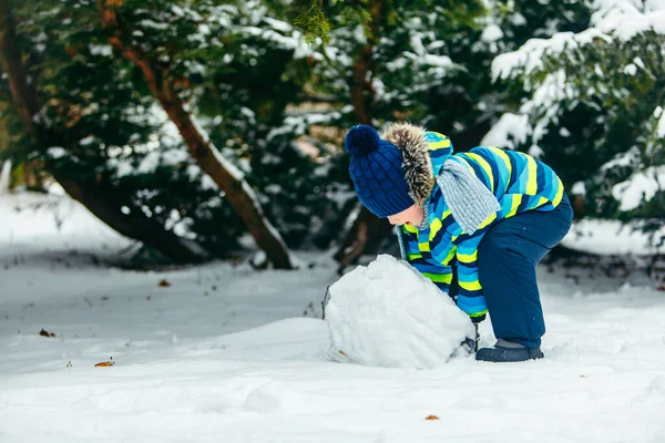 Kleine schattige jongen die sneeuwman maakt. rollen grote sneeuwbal — Stockfoto