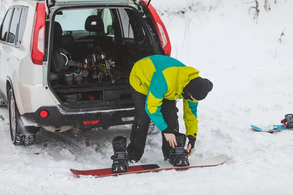 Férfi cserél rendszeres csizma snowboard a parkolóban autó közelében — Stock Fotó