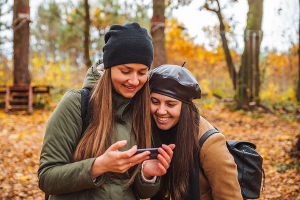 Two pretty women taking selfie picture on phone outdoors at autumn city park — Stock Photo, Image