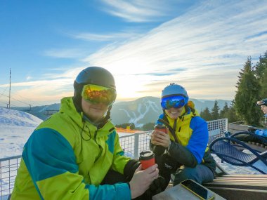Çift tepenin üstünde dinleniyor ve sıcak çay içiyor. Snowboard kayağı