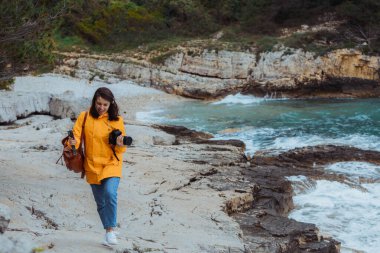 sahil kenarında yürüyen ve sarı yağmurluklu manzara çekim kadın.