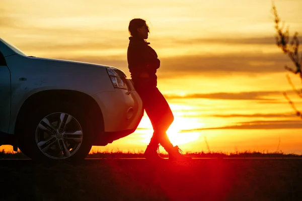 Γυναίκα στέκεται κοντά στο ηλιοβασίλεμα αυτοκίνητο στο παρασκήνιο. οδικό ταξίδι — Φωτογραφία Αρχείου
