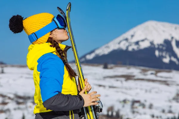 Jovem sorrindo bonita mulher segurando esqui. montanhas no fundo — Fotografia de Stock