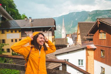 Hallstatt şehrinde sarı yağmurluk giymiş gülümseyen genç bir kadının portresi.