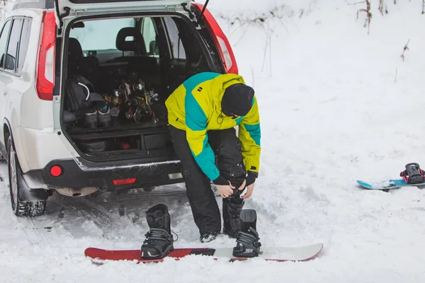 Férfi cserél rendszeres csizma snowboard a parkolóban autó közelében — Stock Fotó