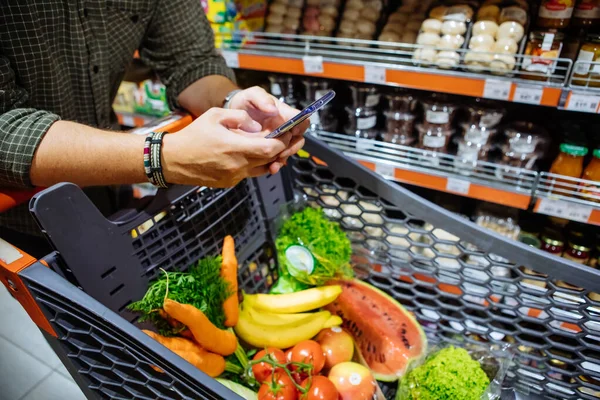 Hombre con teléfono inteligente hacer compras en la tienda de comestibles — Foto de Stock