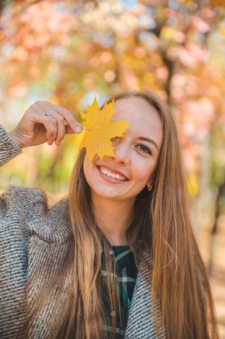 young pretty woman fooling around with yellow maple leaf