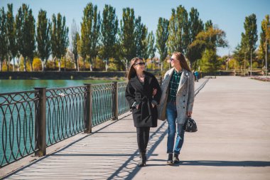 two girlfriends walking by city quay in coats autumn fashion