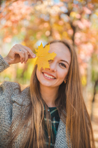 молодая красивая женщина валяет дурака с желтым кленовым листом
