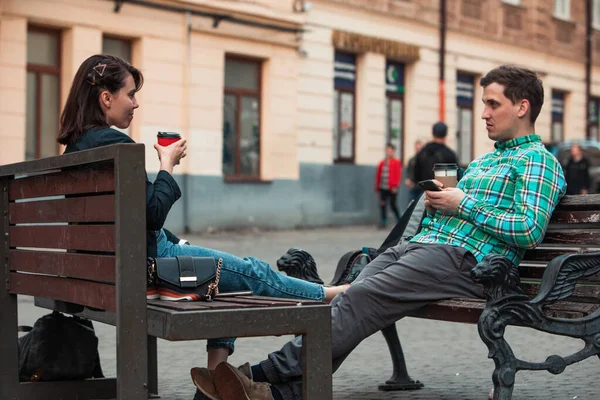 Laughing talking man with woman sitting on bench drinking coffee surfing in internet. urban lifestyle — Stock Photo, Image