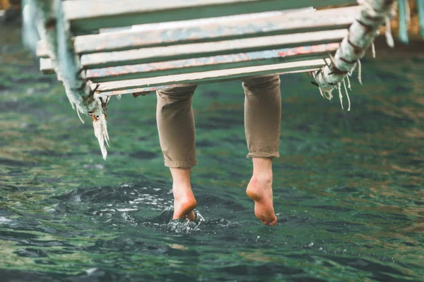 Colheita imagem homem sentado na ponte de suspensão colocar pernas na água do mar — Fotografia de Stock