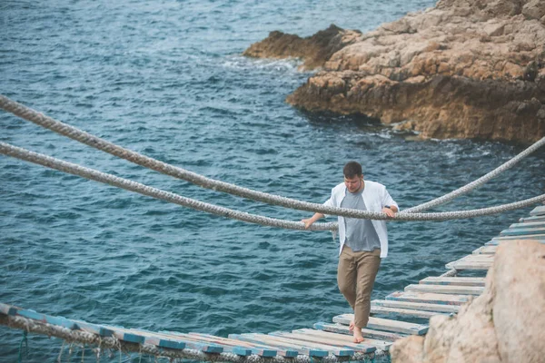 Homem andando por ponte suspensa atravessar baía do mar — Fotografia de Stock