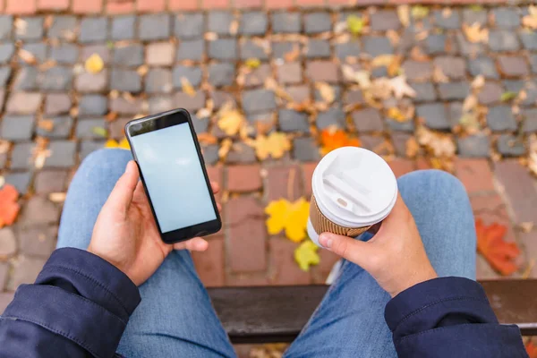 Ningún hombre de la cara sentado en el banco en el parque de la ciudad bebiendo café surfeando por teléfono — Foto de Stock