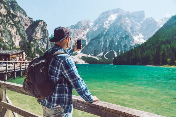 Hombre tomando fotos en su teléfono del lago en las montañas — Foto de Stock