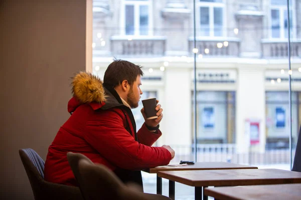 Man in cafe in red winter coat drinking tea warming up — Stock Photo, Image