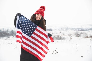 Kırmızı şapkalı genç bir kadın ABD bayrağını tutuyor. Kış zamanı
