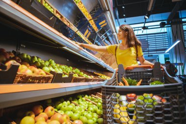 süpermarket mağaza rafından elma alan kadın