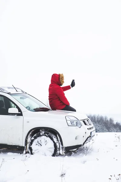 Homem sentado no capô do carro e fotografar da bela vista de inverno em seu telefone — Fotografia de Stock