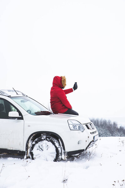 man sitting on car hood and shooting picture of beautiful winter view on his phone