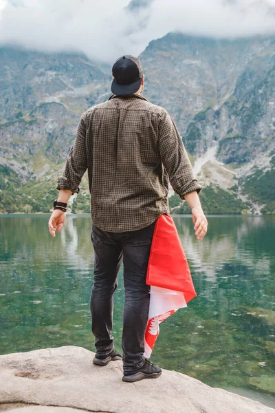Homme debout au bord regardant le lac dans les montagnes tatra avec drapeau poland dans la poche — Photo