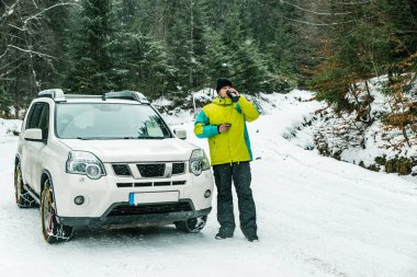 Tekerlekli zincirle SUV arabasının yanında duran bir adam. Biraz ara ver, çayını iç.