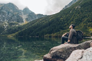 man sitting on the rock in front of lake in mountains enjoying the view