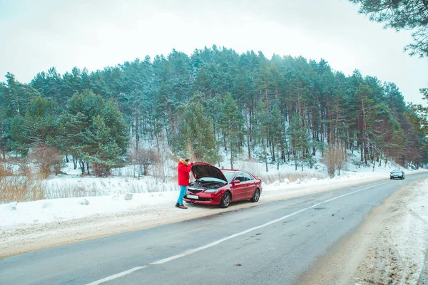 Человек, стоящий рядом со сломанной машиной на обочине дороги в снежную зимнюю погоду — стоковое фото