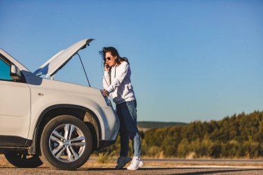 Gün batımında kaputu açık duran bir kadın telefon fotokopi odasında konuşuyor.
