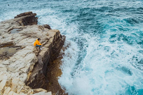 Mulher sentada na borda do penhasco olhando em ondas grandes — Fotografia de Stock