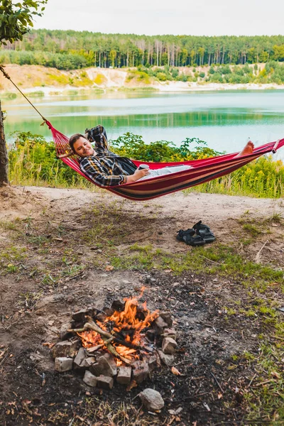 Man som ligger på hängmatta vid sjön stranden nära lägereld — Stockfoto