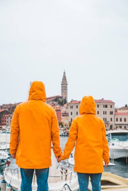 Sarı yağmurluklu çift Rovinj limanında fırtınalı havada yürüyor. Boşluğu kopyala