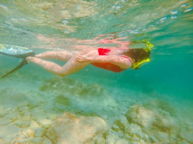 Kırmızı mayo giyen, şnorkel maskeli ve yüzgeçli bir kadın yaz tatili için su altında.