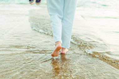 Yaz tatilinde deniz kıyısında koşan beyaz pantolonlu kadın bacakları.
