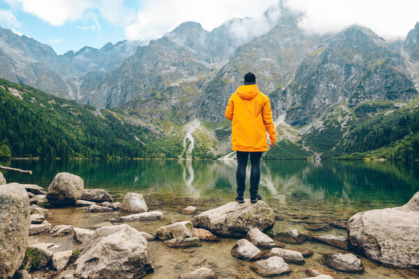 Человек в жёлтом плаще смотрит на озеро в горах
