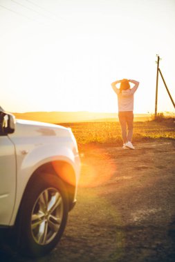 Kırsalda günbatımının tadını çıkaran bir kadın. Beyaz bir cipin yanında duruyordu. Yol gezisi
