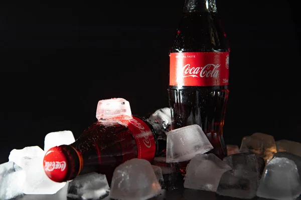 Lviv, Oekraïne - 21 mei 2020: twee glazen flesjes coca cola op zwarte achtergrond in ijs met licht — Stockfoto