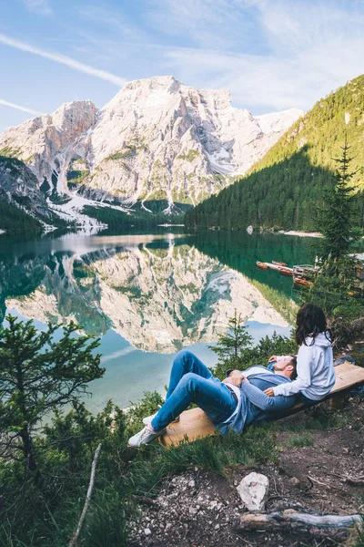 Pár sedí na lavičce a dívá se na jezero v horách — Stock fotografie