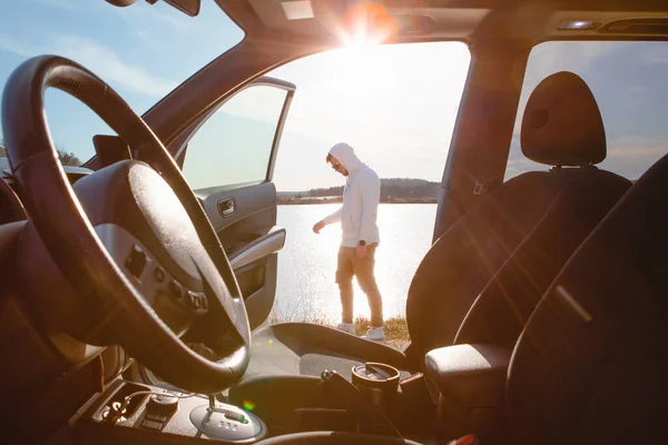 湖に沈む夕日を眺めながら車のそばに立っている男 道路の旅 — ストック写真