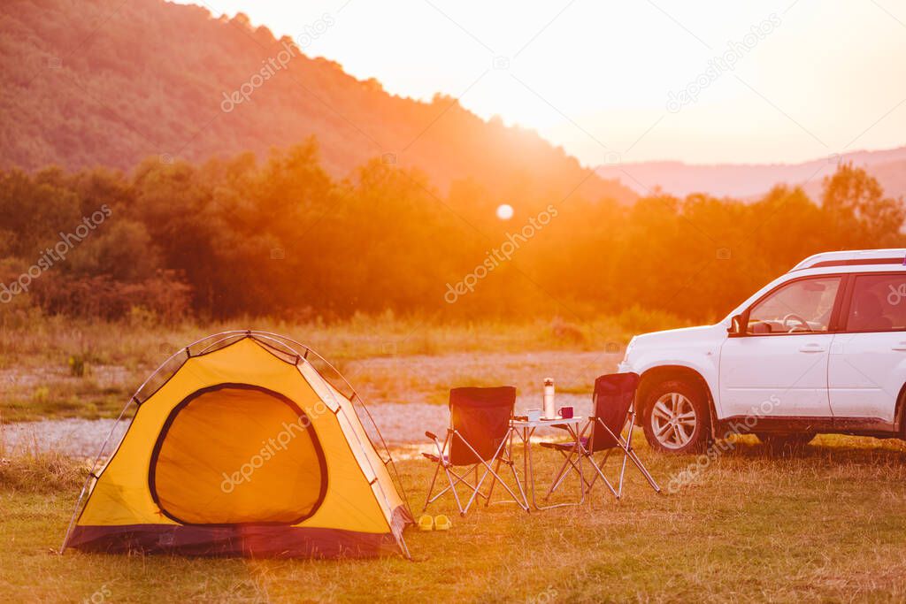 camping at beach of mountain river. suv car. yellow tent. camp table and chairs. copy space