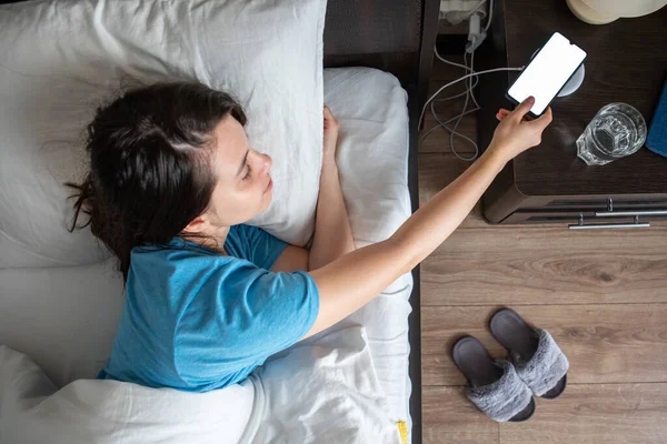 Awake Woman Taking Phone Wireless Charger Bedside Table Overhead Top — Stock Photo, Image